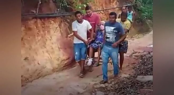 Família usa cadeira para transportar idosa de 91 anos em estrada de terra a caminho do hospital