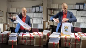Abertura das atas do ínquerido de beatificação do Padre Cícero. Mostra um homem com os papeís na mesa abrindo com uma tesoura os envelopes