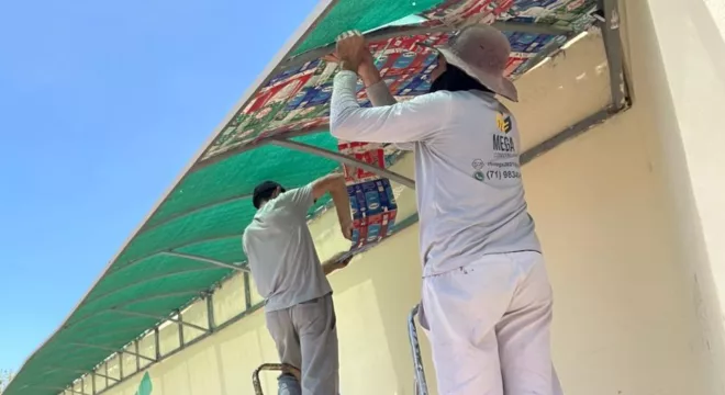 projeto cuca fresca no ponto de onibus do ifce em juazeiro do norte. a imagem mostra dois homens aplicando as mantas na parada de onibus.