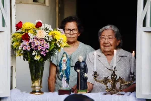 janela com um altar construido com estátuas de santos, em juazeiro do norte. atrás das imagens tem duas mulheres.