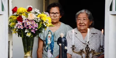 janela com um altar construido com estátuas de santos, em juazeiro do norte. atrás das imagens tem duas mulheres.