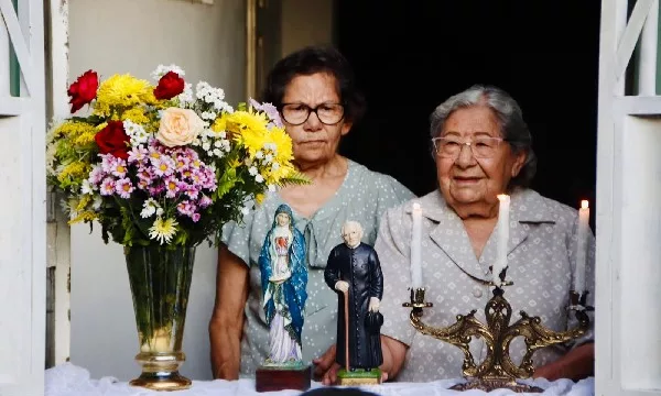 janela com um altar construido com estátuas de santos, em juazeiro do norte. atrás das imagens tem duas mulheres.
