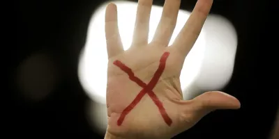Mão com um x vermelho desenhado na palma, representando o pedido pelo fim da violência e feminicídio contra a mulher.
