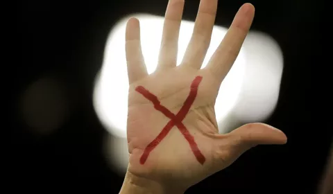 Mão com um x vermelho desenhado na palma, representando o pedido pelo fim da violência e feminicídio contra a mulher.
