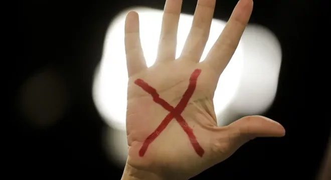 Mão com um x vermelho desenhado na palma, representando o pedido pelo fim da violência e feminicídio contra a mulher.