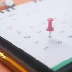 calendário com itens de escritório ao lado e um alfinete marcando uma data.