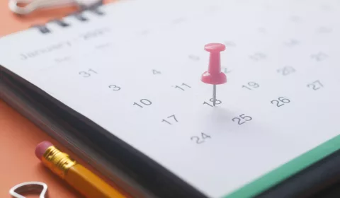 calendário com itens de escritório ao lado e um alfinete marcando uma data.