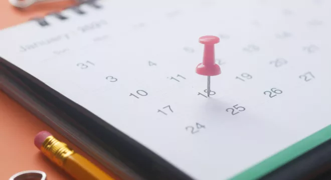 calendário com itens de escritório ao lado e um alfinete marcando uma data.