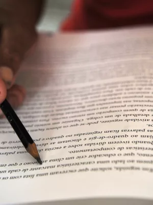 pessoa estudando. a imagem foca em uma página de livro onde a pessoa está segurando um lápis para acompanhar a leitura.